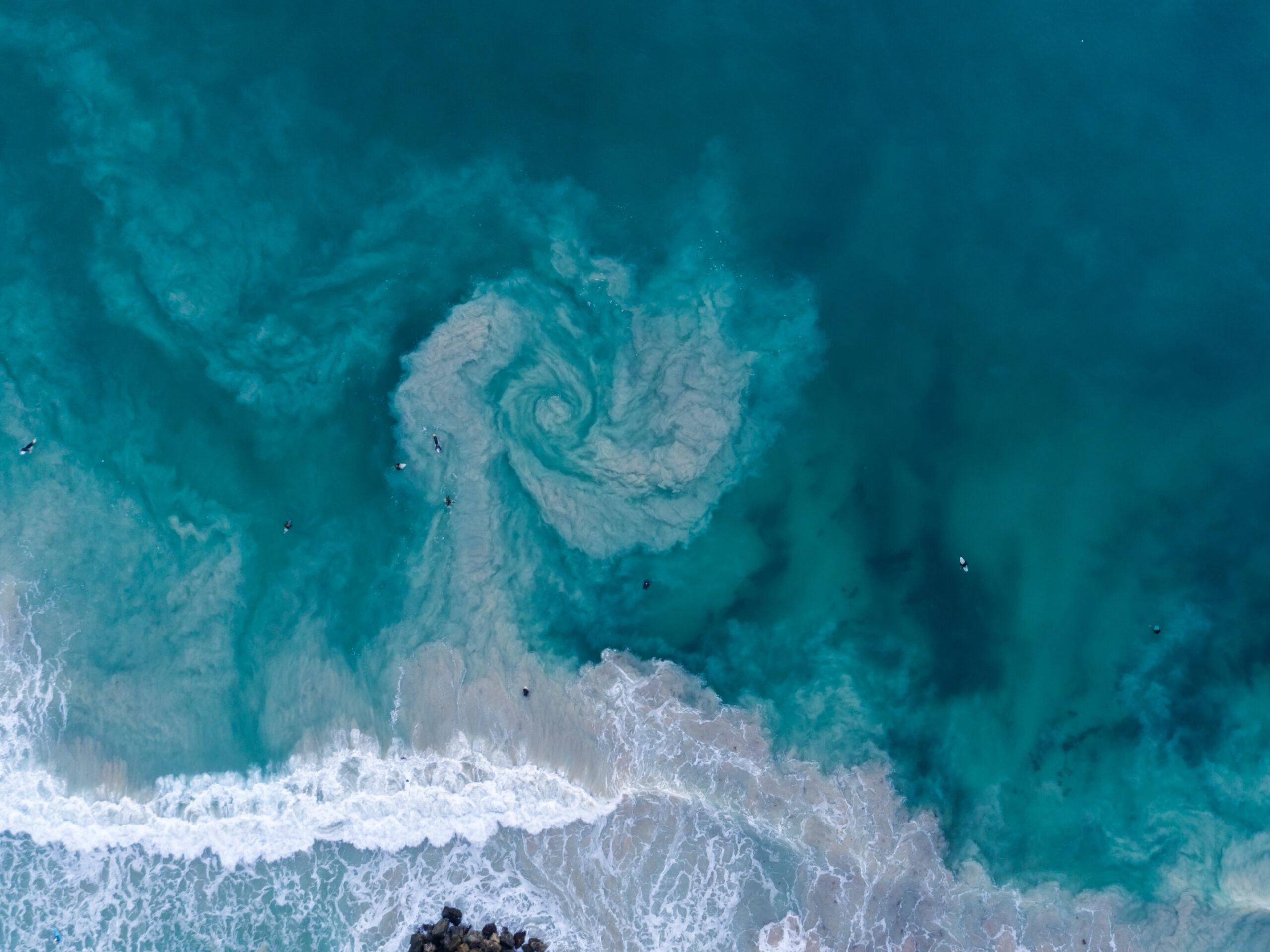 Rip currents occur on surf beaches around the globe. The rocky structure at the bottom of the frame likely contributed to this rip, photographed in Australia and distinguishable by a swirling sediment plume.